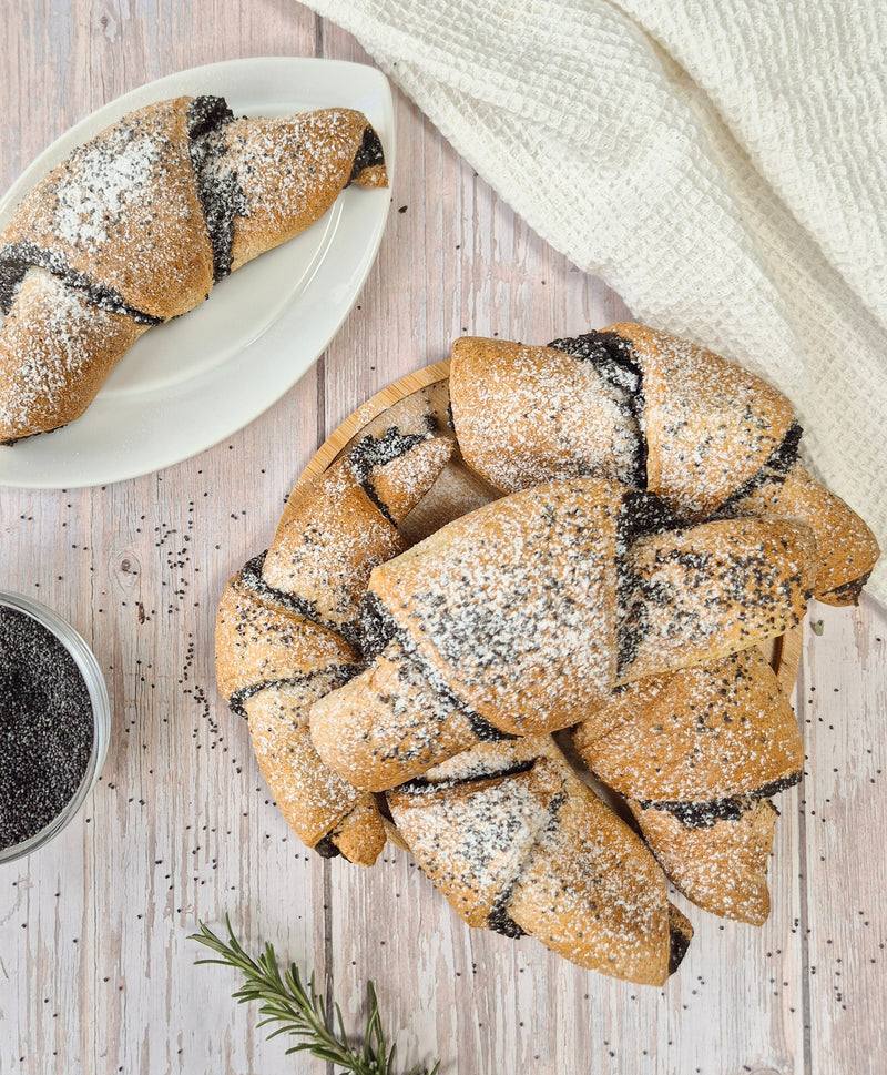 Low-carb Pastries with poppy seeds on a wooden surface with a white cloth and a small bowl of poppy seeds.
