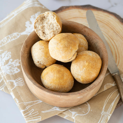 Wooden bowl with low-carb bread rolls on a marble surface with a knife and napkin.