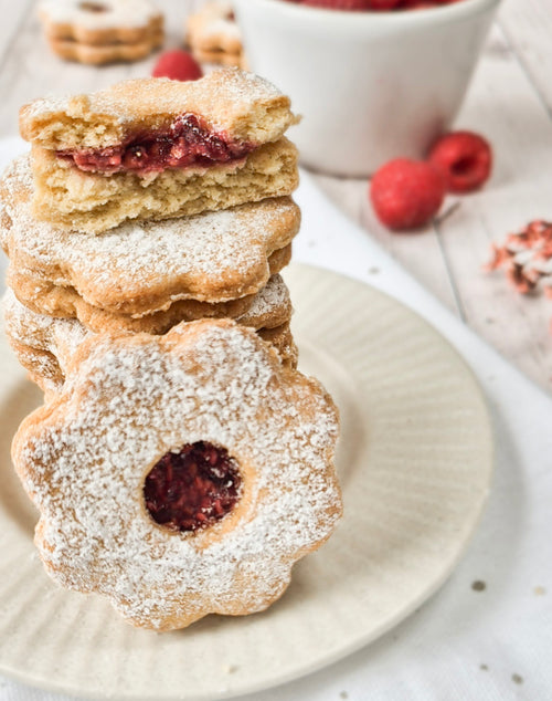Homemade gluten-free linzer cookies stacked on a plate with raspberry filling