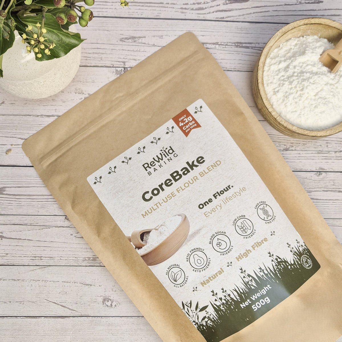Revoliv CoreBake multi-use flour blend package on a wooden surface with a small bowl of flour.