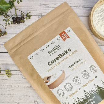 Package of Rewild Baking CoreBake flour on a wooden surface with a bowl of flour and greenery.